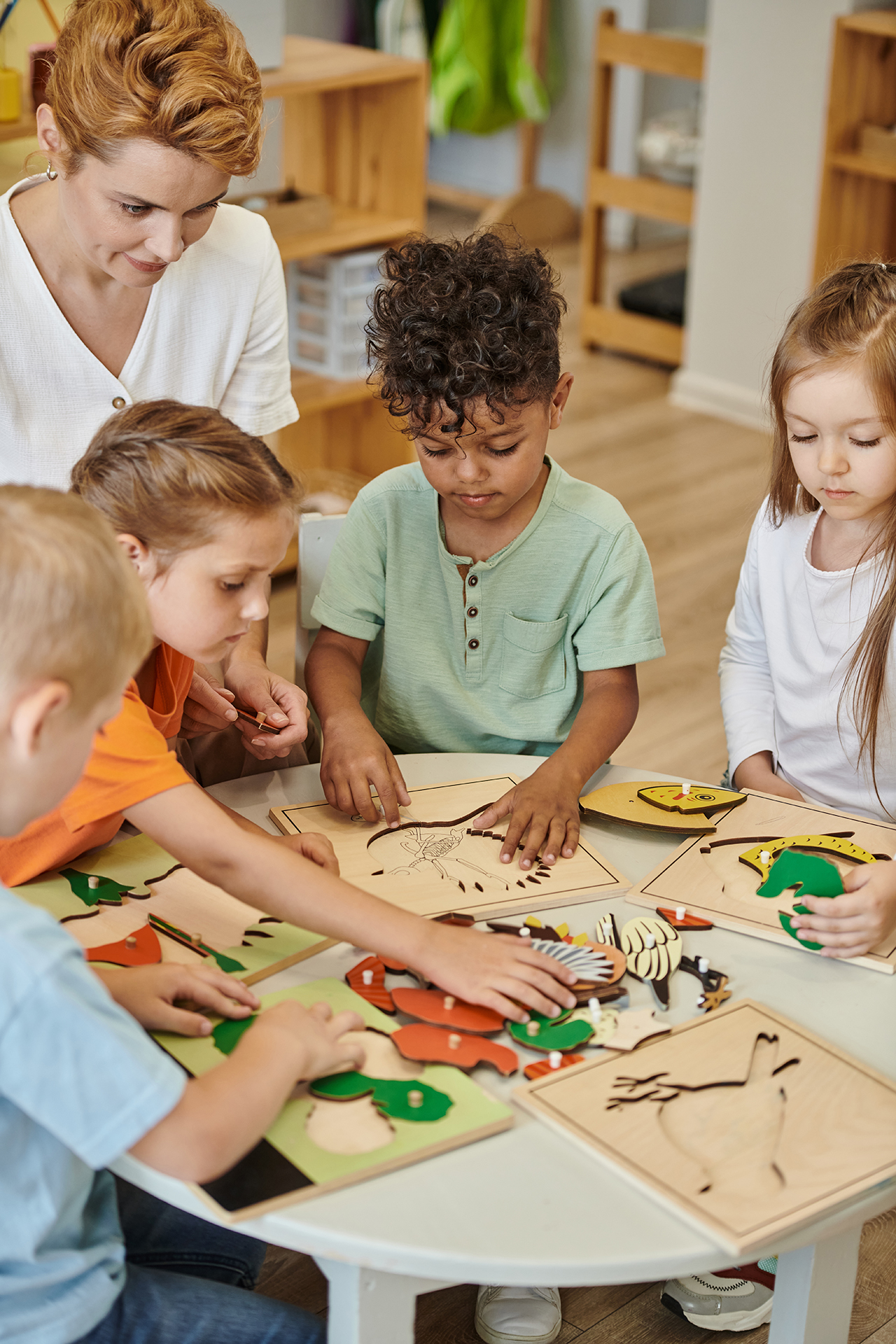 Teacher guides a group of elementary students as they work together on hands-on wooden learning activities at a classroom table.