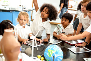 Students exploring wind power and renewable energy using a model wind turbine, tablets and a globe during a classroom STEM activity.